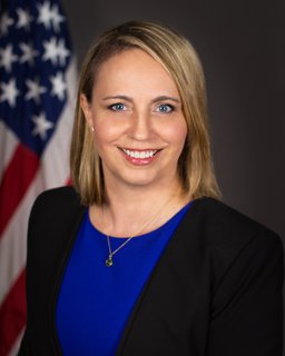 Christi Grimm Headshot on a dark grey background with an American flag