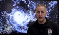 Adam Globerman in front of a satellite photo of a hurricane