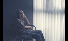 An elderly man in a wheelchair looks up at curtains covering a window